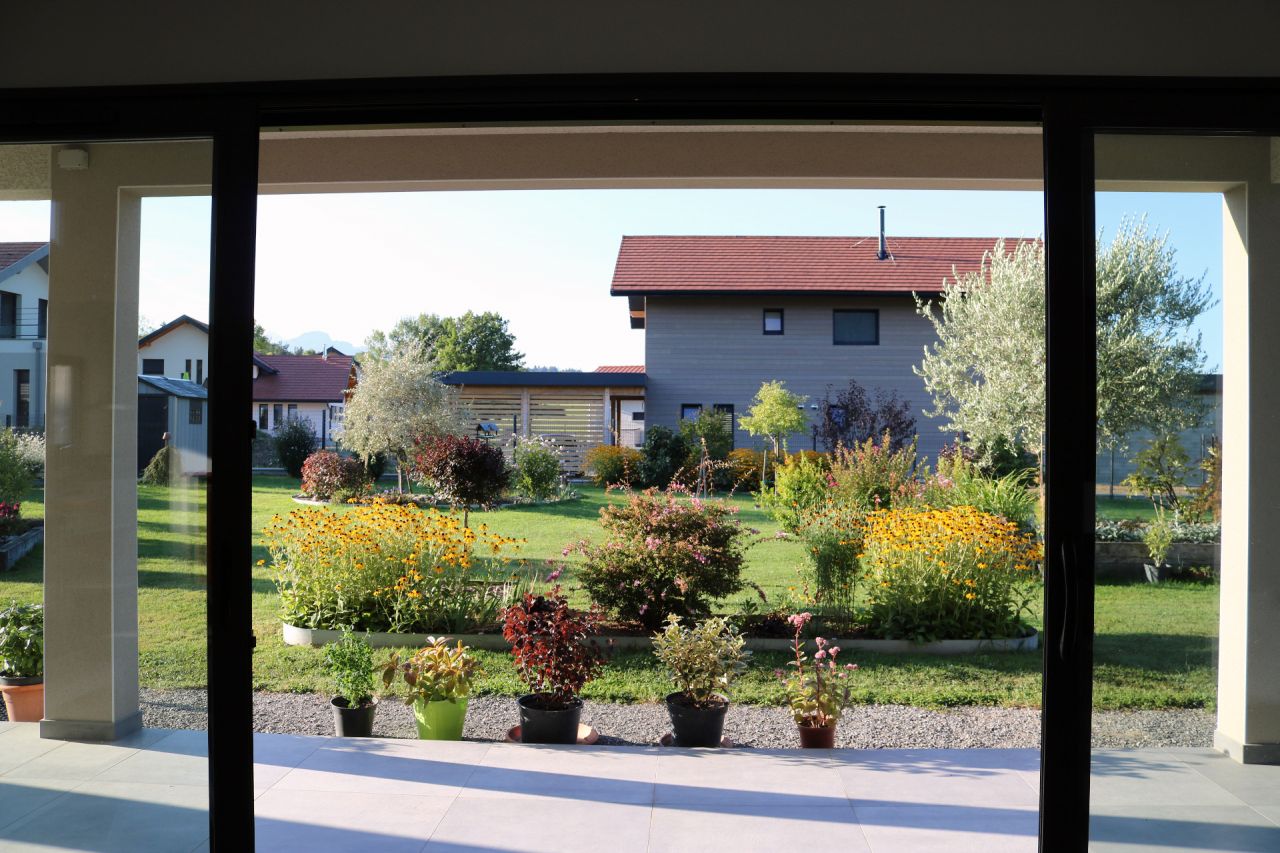 Depuis l'intérieur du salon, l'un des canapés ne regarde pas la télé, mais le jardin, et en entrant dans la maison c'est cette vue qu'on a (porte d'entrée alignée sur la baie principale, au fond)