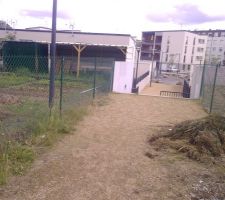 A gauche  de la photo, le jardin communal A traverser. le grillage qui se termine par un mur de soutenement en blanc qui cadre un escalier. 1 regard de 30 x 30 est mis derrière ce mur en bas de la première marche pour aller 35m plus loin se raccorder aux EU public. La conduite EU public passe parallèlement aux 2 1er Blocs de pierre à 6m plus loin.