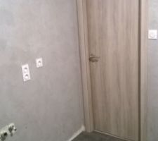 Une petite vue d'ensemble de la salle de bain avec l'enduit terminé et la carrelage de posé et la porte
