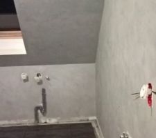Une petite vue d'ensemble de la salle de bain avec l'enduit terminé et la carrelage de posé, et en arrière plan les tuyau d'évacuation a cacher
