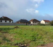 Vue du terrain nu apres fauchage des mauvaise herbes. Piquets montrant l'implantation future de la maison