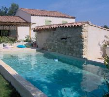 Avant d'attaquer l'aménagement du sous-sol puis l'extension de la maison côté ouest, j'ai réalisé sur le côté est du terrain une piscine reposant sur la restanque haute ainsi qu'un garage attenant à la piscine sur la restanque basse. Malheureusement, j'avais pas les compétences pour une piscine à débordement, mais si c'était à refaire ... 
Mais Madame voulait une piscine bassin.
Une plage immergée prend le volume du bassin sur 1,5 mètre . On a donc sacrifié de la nage pour les jeux des plus jeunes enfants.

Le filtre à sable et les vannes sont protégés dans le garage. Une dérivation après filtration avec une vanne permet de mettre en route la cascade qui sort du mur en pierre collé au mur garage. C'est tout con à faire.