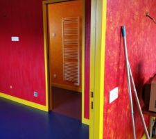 Les travaux de peinture avancent bien. Au fond la salle de bains : sol prune et murs orange. Plan intermédiaire la chambre : sol bleu et murs rouge. Les sols n'ont pas encore reçu la résine. Au premier plan un mur rouge de la salle.