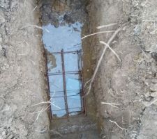 Ferraillage d'un plot de fondation. La ferraille est calée par un éclat de parpaing et est partiellement immergée dans l'eau