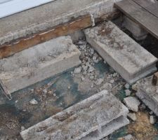 La structure de la terrasse pourrie, sous la baie vitrée (on voit le reste de la lambourde pourrie vissée dans le mur, les parpaings et la bâche dessous)