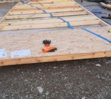 Equerrage du mur. On mesure les diagonales en se fiant au plan du bureau d'étude structure, on tends une sangle de remorque de camion sur la diagonale du mur qui est trop longue, et on tire jusqu'à revenir sur les bonnes mesures.
On va ensuite clouer la plaque d'OSB sous la sangle afin qu'elle tienne cette équerrage, à condition qu'elle ne dépasse pas du bord du mur. Sinon il faudra passer la sangle sous le mur pour pouvoir clouer l'OSB.