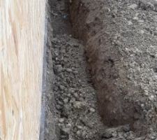 Creusement de la tranchée pour le caniveau sec le long du mur du garage. Avec le mur déjà monté, c'est un peu plus compliqué. Du coup, la tranchée est un peu trop profonde, et il faut terminer de la creuser à la main tout au fond (après le regard).