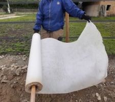 On déroule le géotextile en fond de tranchée. En utilisant un manche de pelle pour le dérouler comme du papier toilette, ça va plus vite (sauf qu'on n'arrache pas les feuilles une par une) !