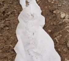 Géotextile en fond de tranchée, il faut le faire tenir avant de remblayer.
