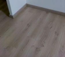 Pose chez un client d'un parquet stratifié dans une chambre de l'étage avec coupe biaisée 45° des angles de plinthes