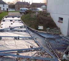 Pose d'un polyane pour éviter que le sable mis précédemment ne pompe trop rapidement l'eau du béton.
Par dessus le polyane, fixation par plot de béton des rails de dilatation et des caniveaux drainant les eaux de ruissellement vers le puisard d'ep avant le caniveau juste devant la porte de garage. (sécurité en cas de forte pluie)