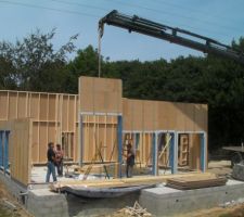 Jour 1 du montage des murs. La taille des panneaux est réduite en raison des contraintes d'accès. On remarque le pilotage de la grue par le professionnel au pied du mur. Facteur d'efficacité.