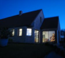 Le sapin illuminé dans la baie d'angle au lever du jour dans la maison éclairée