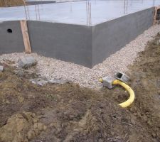 Un drain (tuyau jaune sur la photo) a été placé tout autour des fondations pour collecter les eaux s'infiltrant dans la terre. Une couche de graviers a été déposée par dessus pour éviter que la terre ne vienne obturer les petits trous du drain.