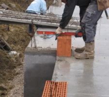 Les briques d'angle sont légèrement différentes de celles qui vont faire les murs Un trou en leur millieu permet de faire passer le ferraillage et d'y insérer par la suite du mortier pour fabriquer comme un pilier