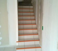 Pose du carrelage en cours dans l'escalier. Les nez de marche sont en ch&ecirc;ne mais prot&eacute;g&eacute;s par un scotch orange.
