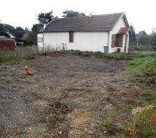 Elle est prise du chemin d'accès et donne en diagonale. On voit le mur du fond du terrain et la limite côté droit qui s'arrête juste avant la maison.