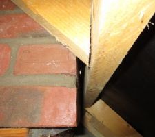 Au centre de la photo, sous la boiserie, à droite des briques, un trou laissant apparaitre la lumière du jour