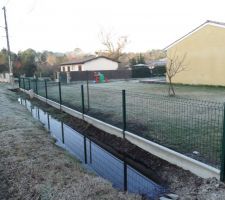 Pose de la cloture en panneaux rigides le long du fossé avec plaques en béton dessous.