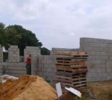 Vue du devant de la maison : On voit l'entrée du garage, et la porte d'entrée est cachée par la pile de palettes.