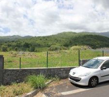 Vue du terrain depuis la rue, notre acces est juste au dessus a droite (pas visible sur la photo, l'entree que l\'on voit est celle de nos futurs voisins).
La montagne en face est non constructible pour le moment.
